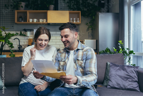 Young family. The man and the pregnant woman received a letter, documents, a mortgage permit, and a loan. Very happy. Sitting on the couch at home. photo