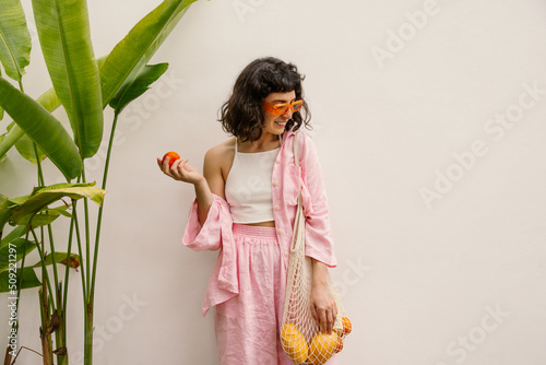 Canvas Print Beautiful young caucasian woman looks away through sunglasses holding shopping pawl standing on white background