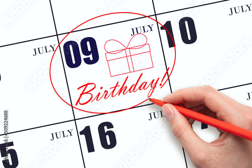 The hand circles the date on the calendar 9July, draws a gift box and writes the text Birthday. Holiday. photo