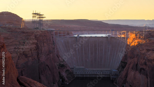 Glen Canyon Dam with Glen Canyon Dam Bridge in front and Lake Powell water surface in the back in the golden hour light. Red cliffs of the gorge and concrete wall of the dam in tranquil scene.