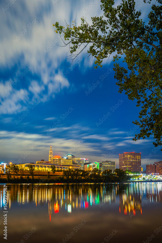 Nightscape of Downtown Hartford in Connecticut with reflections of the lights on the blue water on cloudy dawn.