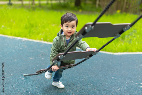Little Asian boy is playing on the wooden playground with happy face in summer outdoors and looking at the camera with a smile