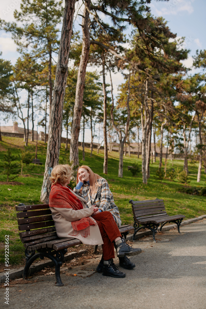 A grandmother is laughing and having fun with her adolescent granddaughter while sitting on the park bench. A grandmother is laughing and having fun with her adolescent granddaughter while sitting on the park bench.