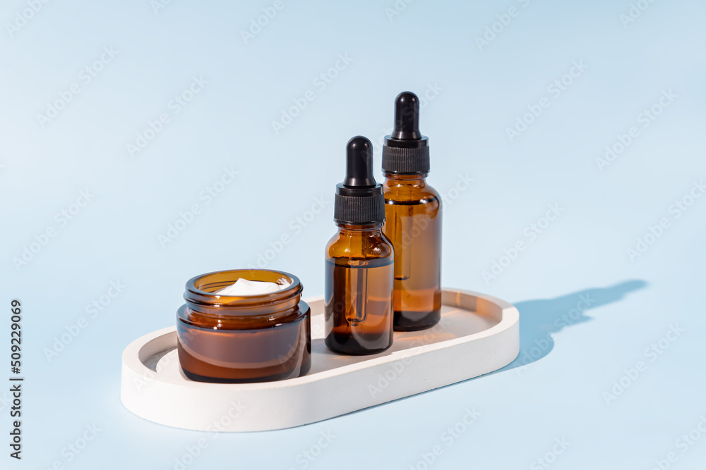 Open cream jar and dropper bottle with face oil on a ceramic tray