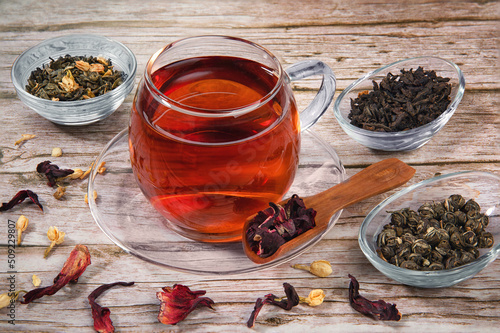 Cup of tea on wooden table with dry herb leaves of different tea.