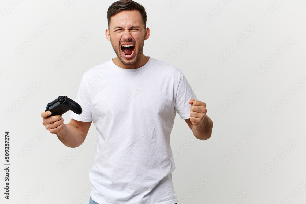 Aggressive angry tanned handsome man in basic t-shirt play difficult game with joystick gamepad posing isolated on over white studio background. Copy space Banner Mockup. Gamer RPG concept Aggressive angry tanned handsome man in basic t-shirt play difficult game with joystick gamepad posing isolated on over white studio background. Copy space Banner Mockup. Gamer RPG concept