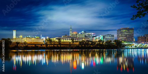 Nightscape and cityscape of downtown Hartford in Connecticut with glowing bokeh light reflections on the river water on a cloudy night.