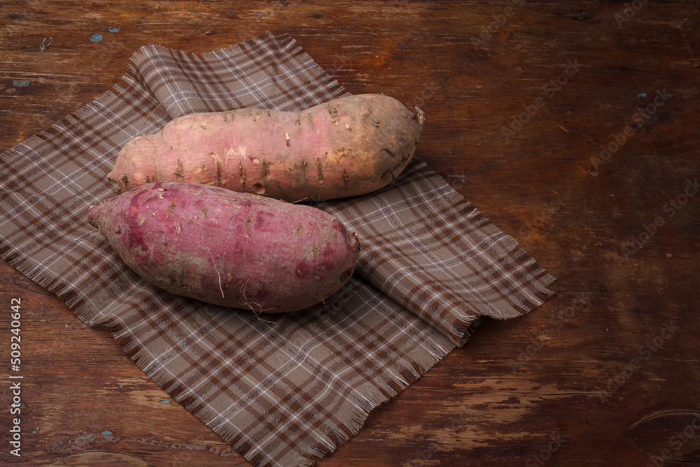 Orange, purple raw sweet potatoes, yam on wooden rustic table, fabric napkin. Farm harvest, organic vegetables, shop local vegan food Orange, purple raw sweet potatoes, yam on wooden rustic table, fabric napkin. Farm harvest, organic vegetables, shop local vegan food