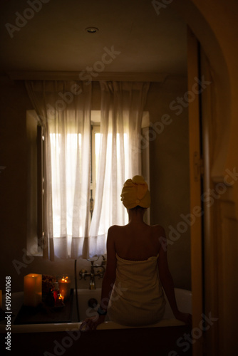 Slim white woman with long hair in the bath room with window. White towel on the body. Morning time.