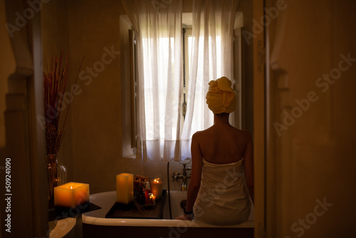 Slim white woman with long hair in the bath room with window. White towel on the body. Morning time.