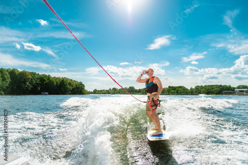A man on a wakeboard being pulled behind a boat finishes a drink on a hot summer day on a Minnesota lake. Copy space