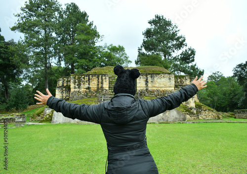 Mujer latina con los brazos abiertos mirando hacia un templo en las Ruinas de Iximche en Guatemala. photo