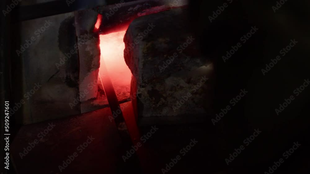 The blacksmith takes out a billet of red-hot metal from a gas furnace. The blacksmith takes out a billet of red-hot metal from a gas furnace.