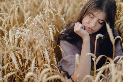 Fotografiet Stylish calm woman sitting in wheat field in evening light