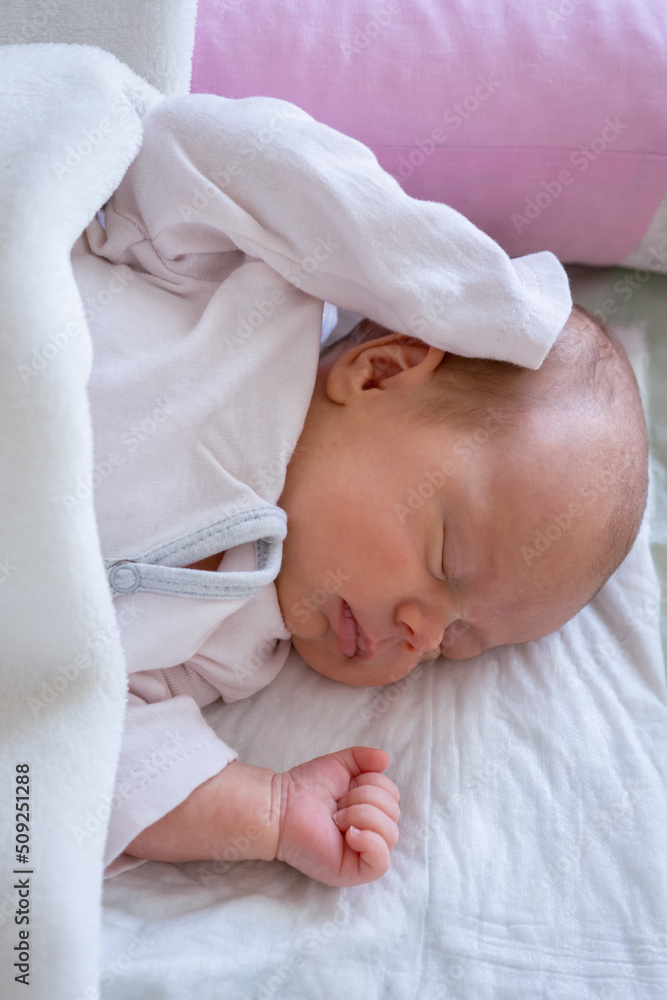 cute little newborn baby girl peacefully sleeps in the nursery on a white cotton bed. vertical cute little newborn baby girl peacefully sleeps in the nursery on a white cotton bed. vertical