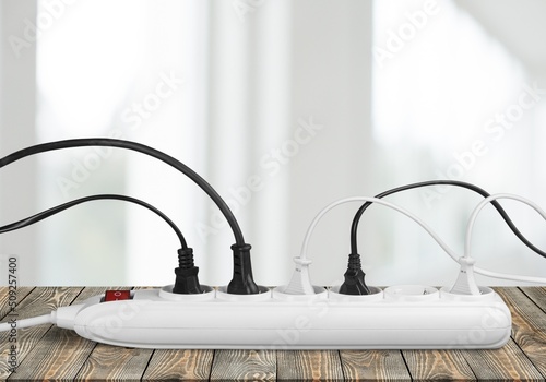 Unplugged electric appliance plug over switched off white power strip on the floor. Increasing the energy costs, heating costs, save electricity concepts.