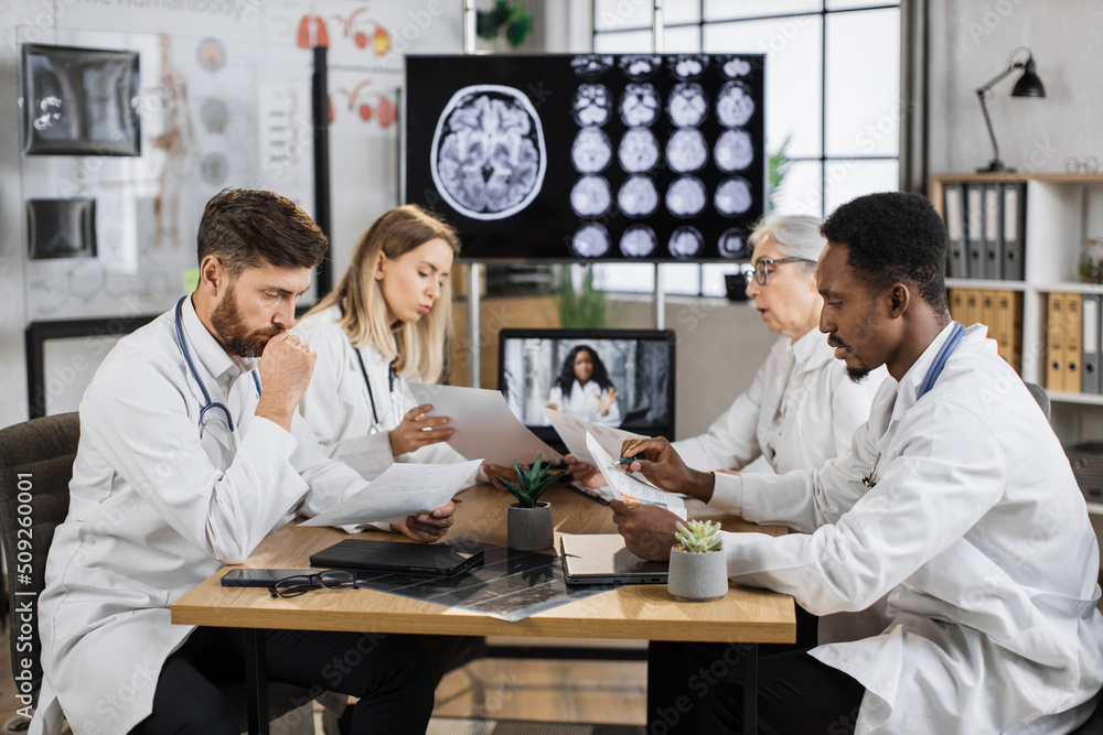 Teamwork of diverse neuroscientists sharing lists with researchings while discussing disease problems in science laboratory. Healthcare workers using monitor with x ray scan showing brain anomalies. Teamwork of diverse neuroscientists sharing lists with researchings while discussing disease problems in science laboratory. Healthcare workers using monitor with x ray scan showing brain anomalies.