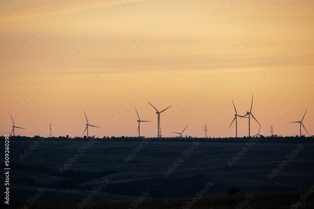 Windmills generating energy in field. Windmills on background of yellow clouds.