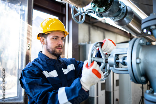 Industrial worker closing valve of gas pipeline inside heating plant.