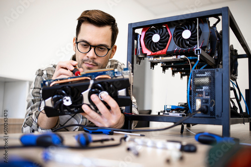 Caucasian man expert changing cooling fans on graphics card and maintaining bitcoin mining rig.
