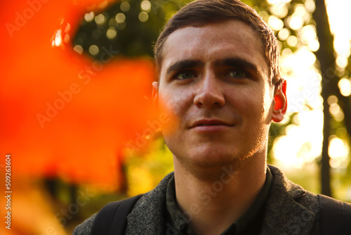 Portrait young man on nature autumn background. Serious young man. 20s years. Handsome man outdoors portrait. Orange colored. Walking in park