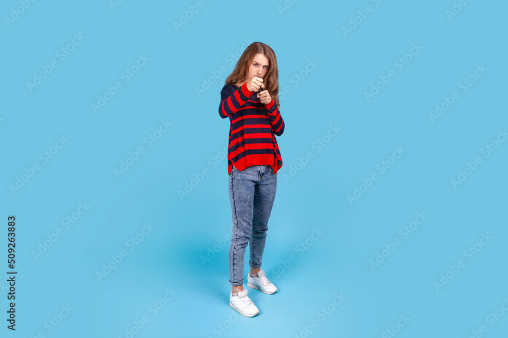 I'll hit you! Full length portrait of aggressive woman standing with raised fists boxing gesture, ready to punch, ready to struggle, fighting spirit. Indoor studio shot isolated on blue background. I'll hit you! Full length portrait of aggressive woman standing with raised fists boxing gesture, ready to punch, ready to struggle, fighting spirit. Indoor studio shot isolated on blue background.