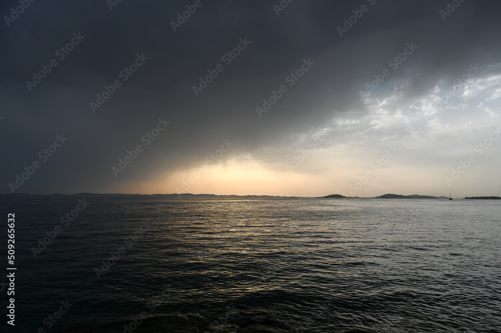 Obraz premium Waves on the sea with dramatic clouds above at sunset. Stormy weather at the sea, view from a boat. Rainy summer day. 