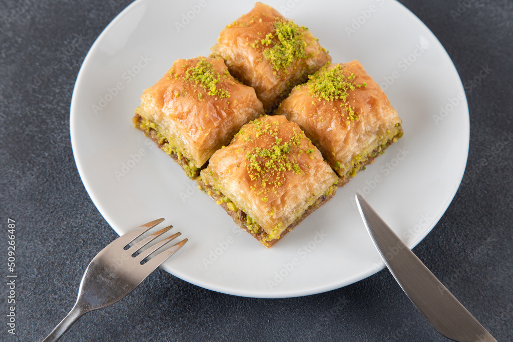 Pistachio baklava on a white plate.A plate of traditional baklava on a dark background Pistachio baklava on a white plate.A plate of traditional baklava on a dark background