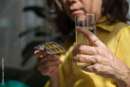 Elderly woman with pills and glass of water in her hands. Age, medicine and healthcare concept.