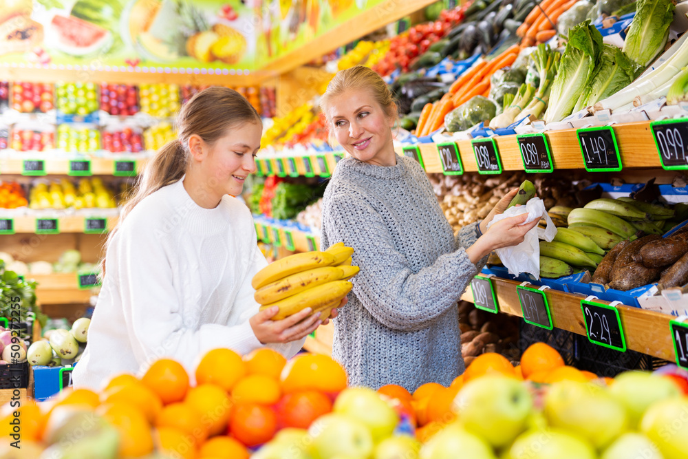 Portrait of teenage girl and her mother who buying fresh vegetables and fruits at grocery shop