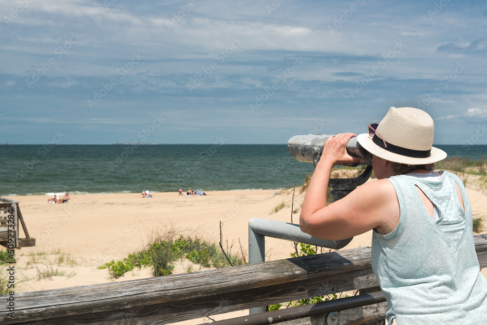woman in  hat looks through Coin binoculars at ocean.