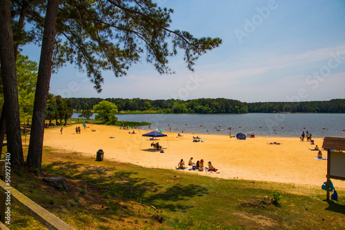 a gorgeous summer landscape at the beach with people sitting in the sand and playing in the vast blue water of Lake Acworth surrounded by lush green trees and blue sky at Cauble Park in in Acworth photo