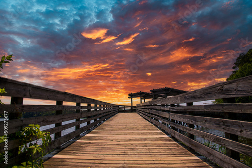 a brown wooden bridge over the silky green waters of Lake Acworth surrounded by lush green trees and plants with powerful clouds at sunset at Cauble Park in Acworth Georgia USA photo