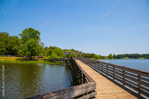 a brown wooden bridge over the silky green waters of Lake Acworth surrounded by lush green trees and plants with blue sky and clouds at Cauble Park in Acworth Georgia USA photo