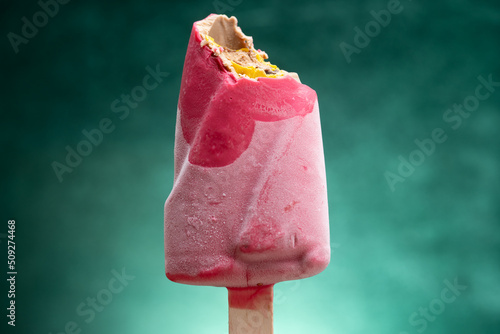 pink color chocolate outer popsicle with some bites on a gradient green background