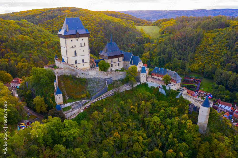 Aerial view of large Gothic Karlstejn Castle on top of hill against background of Czech village near Prague..