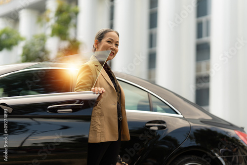 Portrait of Asian Senior Business woman step out luxury car while come to office. Account and Finance concept. © itchaznong