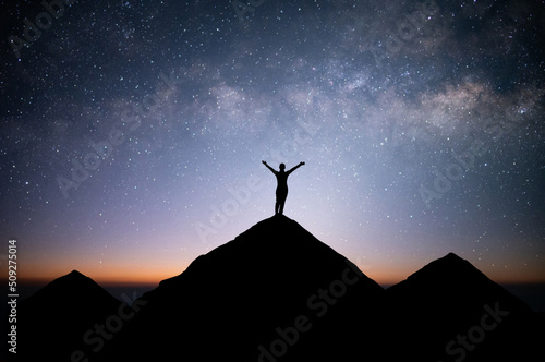 Silhouette of young female traveler and backpacker standing and watched the star and milky way alone on top of the mountain. She enjoyed traveling and was successful when he reached the summit.