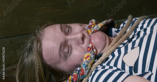 Young blonde woman in a striped t-shirt is lying on the floor bound and gagged. She is twitching and trying to get away, close up. Kidnapping is illegal. Friendly prank