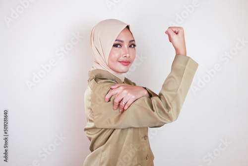 Gorgeous strong young Muslim Asian woman wearing a brown uniform and showing biceps and smiling. Indonesian girl strong concept.