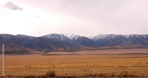 Large desert steppe at the foot of snow-covered mountain ranges in early autumn.