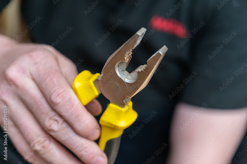 The hand of a mature man holding the Pliers. Hand-held locksmith's tool.