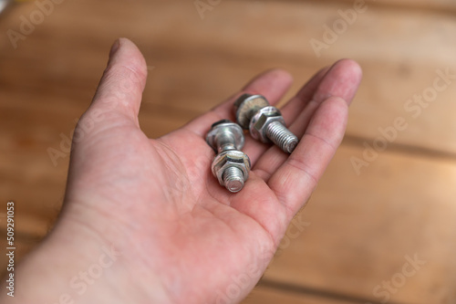 Bolts and nuts lie in the palm of my hand. Two silver bolts with screwed-on nuts lie in the hand of a middle-aged man. A first-person view. Selective Focus.