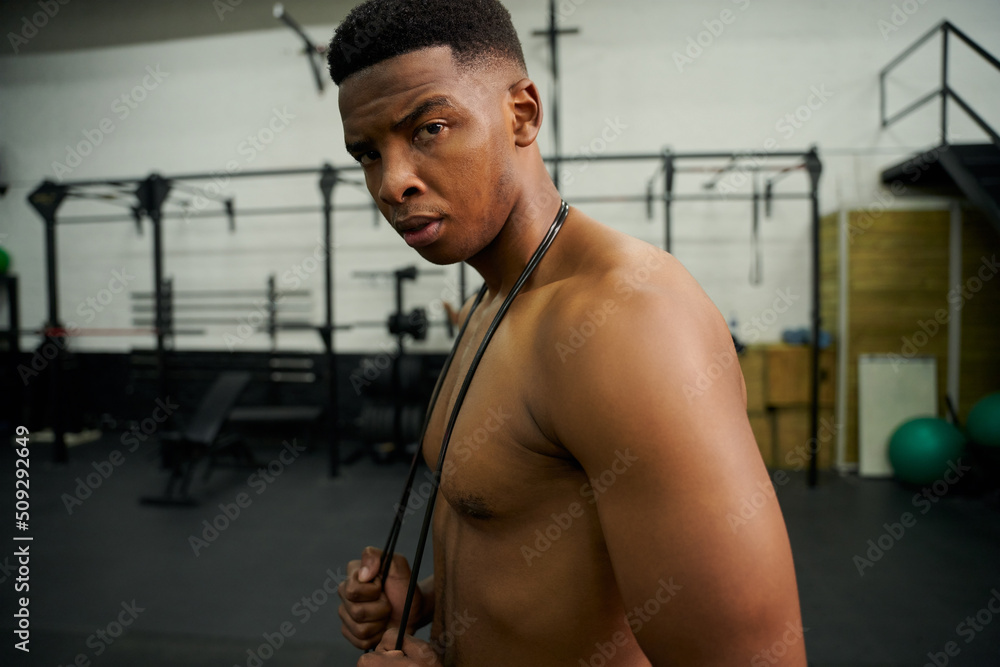 African American male holding skipping rope in the gym. Male athlete looking to the camera during exercise. High quality photo African American male holding skipping rope in the gym. Male athlete looking to the camera during exercise. High quality photo