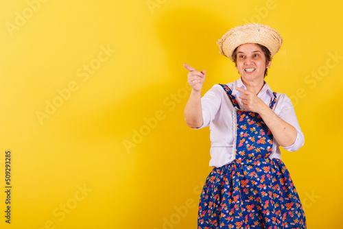 Mature woman dressed in typical Festa Junina clothes. Pointing at something in the distance, looking indicating. photo