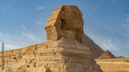 Sculpture of the great Sphinx against the blue sky and the pyramid of Menkaure. The layered structure of the ancient statue is visible. Close-up. Profile view. Egypt