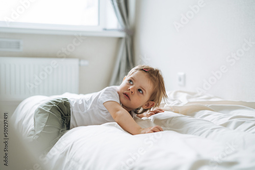 Cute funny baby girl in home clothes lies on bed at home