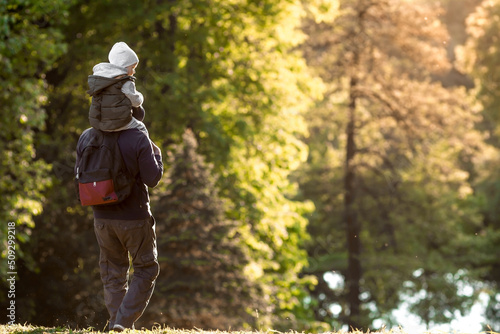 A man and a boy go hiking in the summer forest with a backpack for hiking. Portrait of a father and son sitting on his father's shoulders in the forest at sunset. The concept of travel.