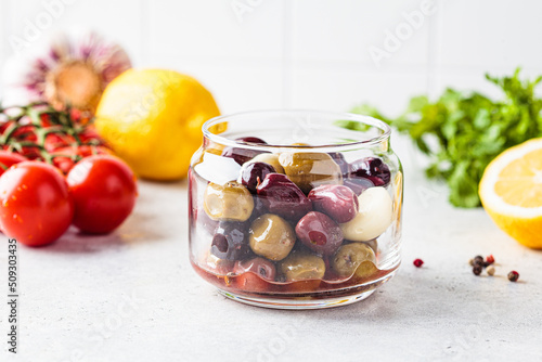 Marinated olives with spice and oil in jar, white kitchen background. photo