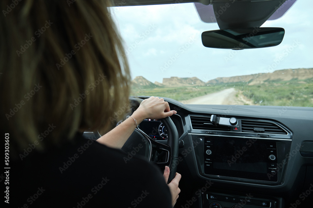 Woman driving a car while traveling on the desert road with a rocky landscape in the background. road trip vacation